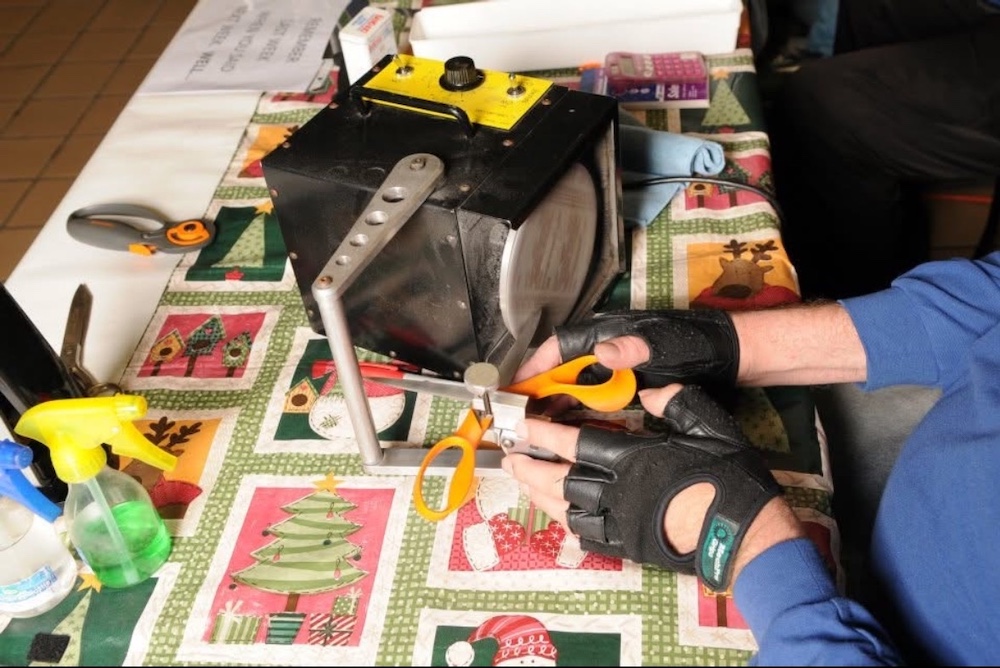 Andrew sharpening a pair of scissors on his work bench at The Way Sharpening.